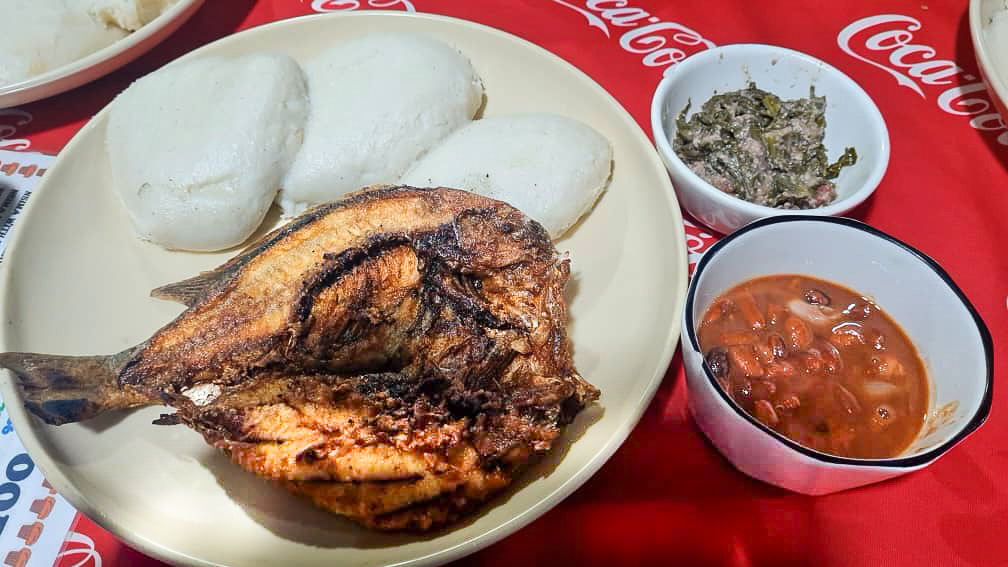 a plate with a traditional Malawian meal of fish, nsima, relish, and beans on a coca-cola table mat.