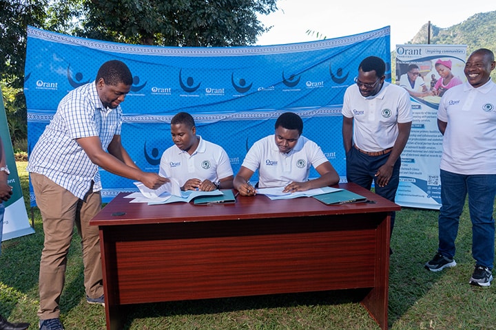 Five members of the staff of Orant Charities Africa and Opulence Malawi stand around a wooden desk as they prepare the MOU paperwork.