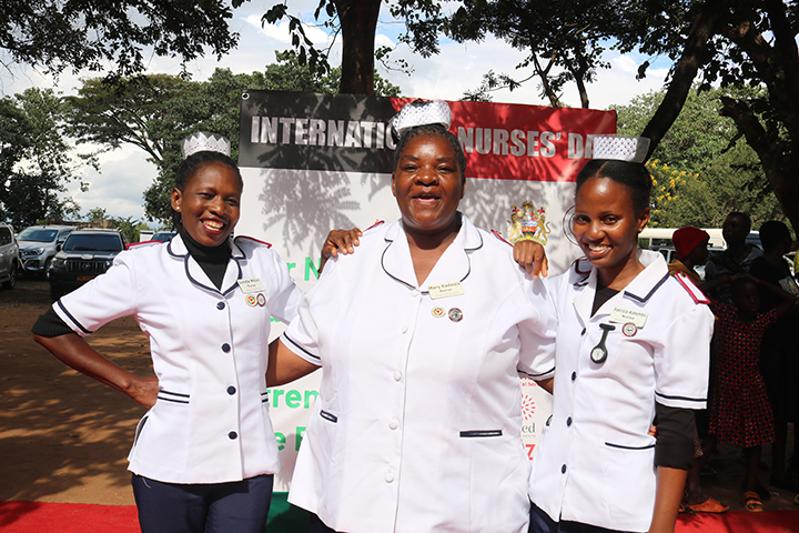 Three nurses join arms together, wearing white jackets and white hats