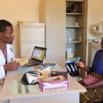 A physician speaks with a patient across a desk in the clinic room of Orant's Non-Communicable Disease Clinic.
