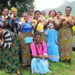 A group of African women hold up paper money in their hands. They are smiling and happy.
