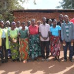A group of people stand together in front of a mud brick building.