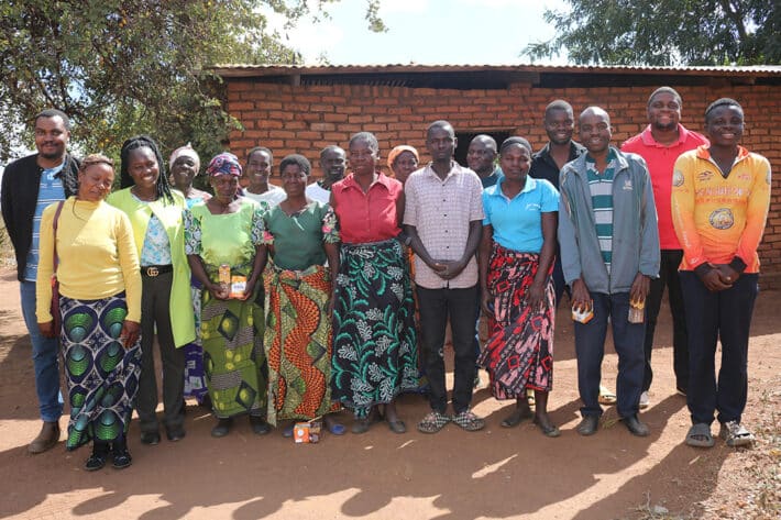 A group of people stand together in front of a mud brick building.