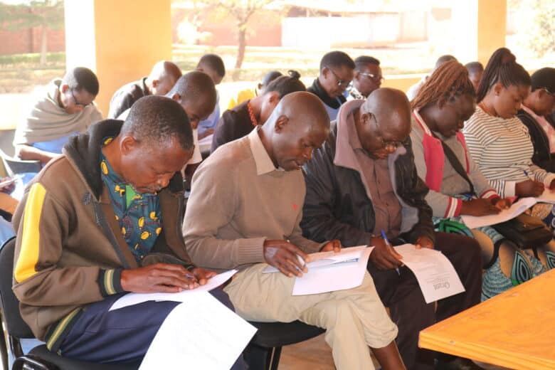 Many people sitting in chairs taking notes in notebooks on their laps