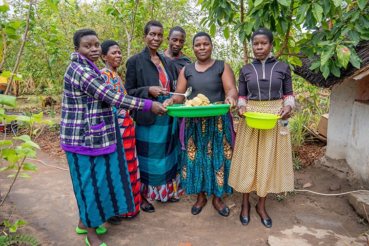 Several African women stand together holding bowls of food.