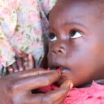An African Baby receives vitamin A supplementation through a small ampule through its mothers hand.