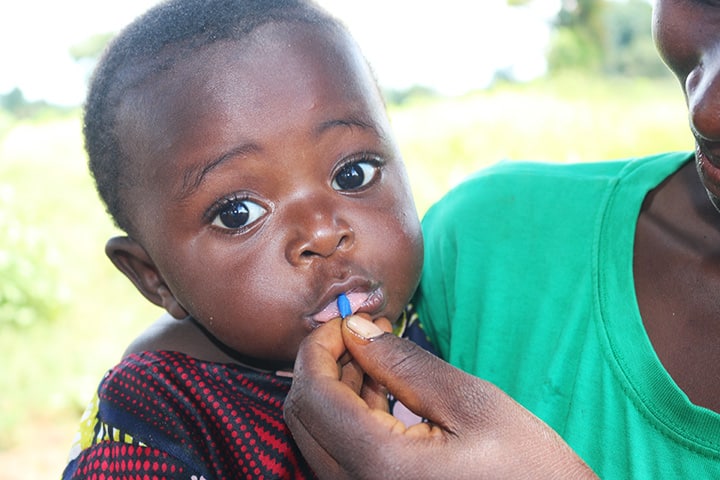 An African baby looks at the camera while it receives a supplement of medicine from its mother's hand.