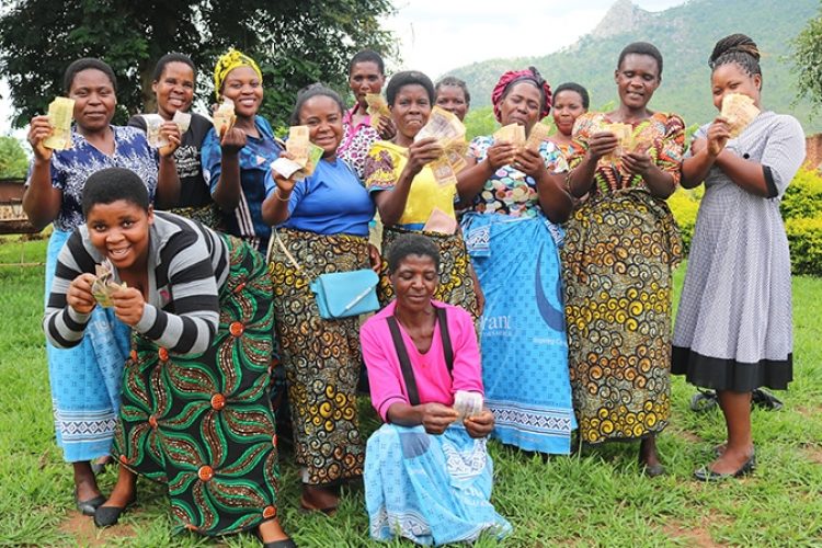 A group of African women hold up paper money in their hands. They are smiling and happy.