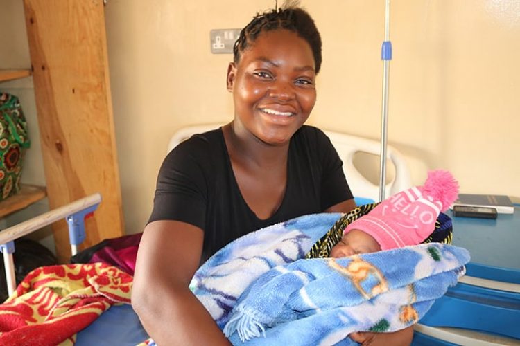 An African woman holds her newborn baby, which is wrapped up in warm blankets. The mother has a big smile.